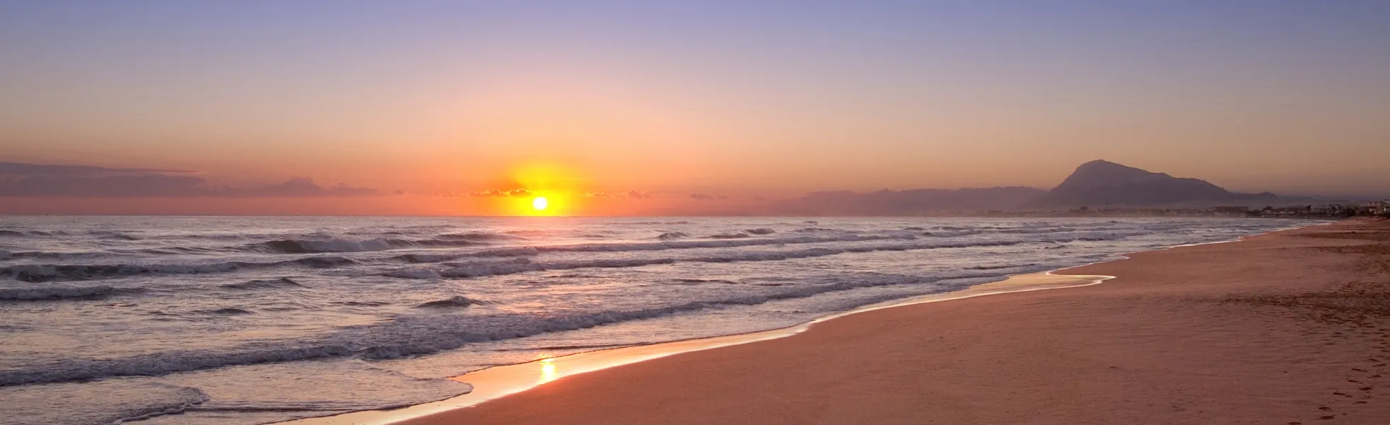 Amanecer sobre la orilla de la playa con la montaña al fondo