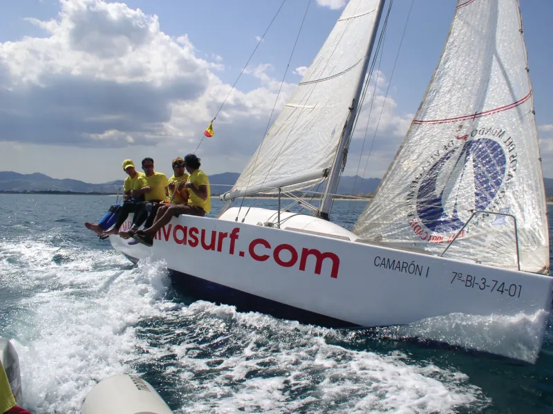Velero navegando escorado con los tripulantes sentados en la banda
