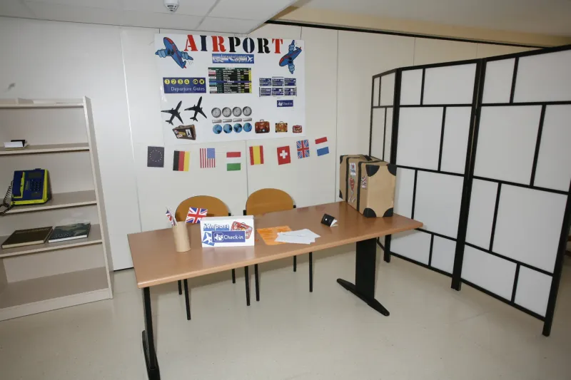 Aula ambientada como mostrador de aeropuerto con banderas y paneles de vuelos