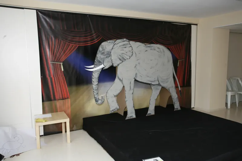 Escenario del aula de teatro con decorado de elefante y telón rojo