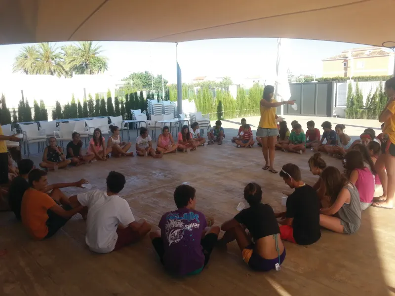 Alumnos sentados en círculo en la terraza atienden a una monitora