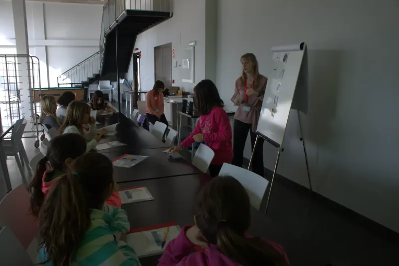 Profesora explica en la pizarra mientras los alumnos siguen la clase