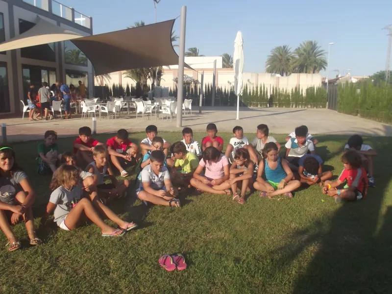 Grupo de alumnos sentados en el césped al atardecer junto a la terraza