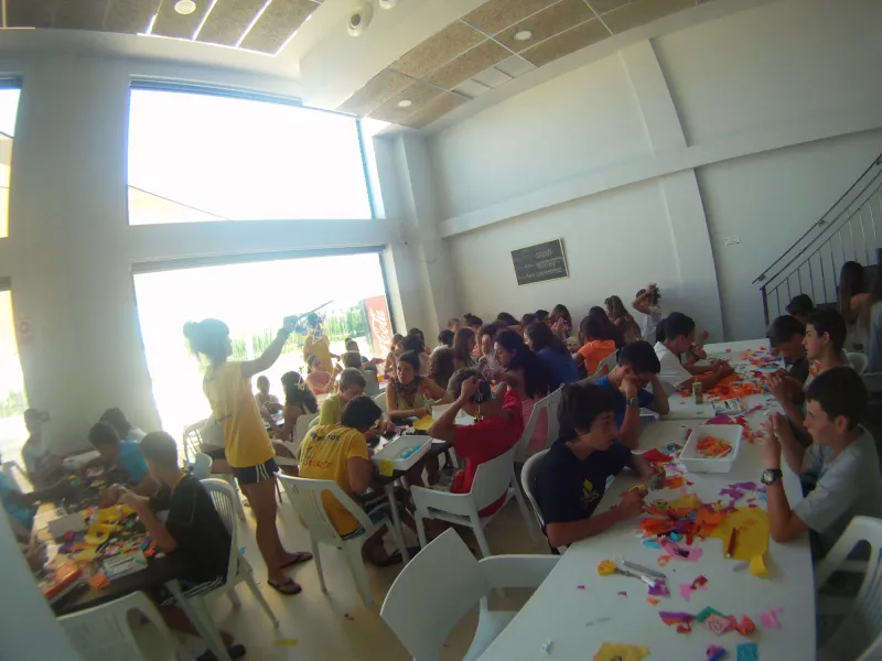 Alumnos hacen manualidades con papel de colores en un salón acristalado