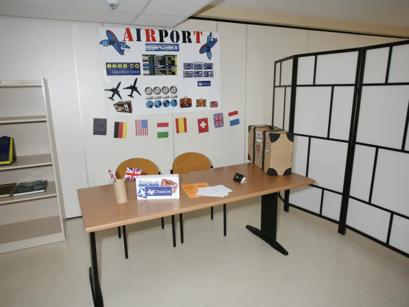 Aula ambientada como mostrador de aeropuerto con banderas y paneles de vuelos