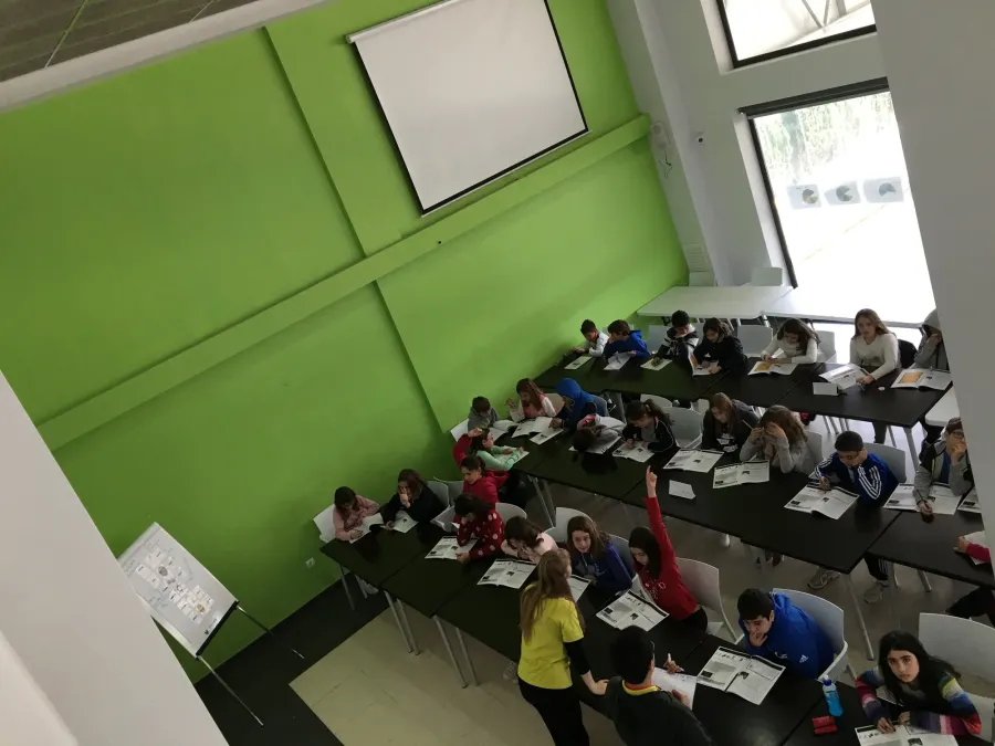 Vista desde arriba de una clase con alumnos levantando la mano