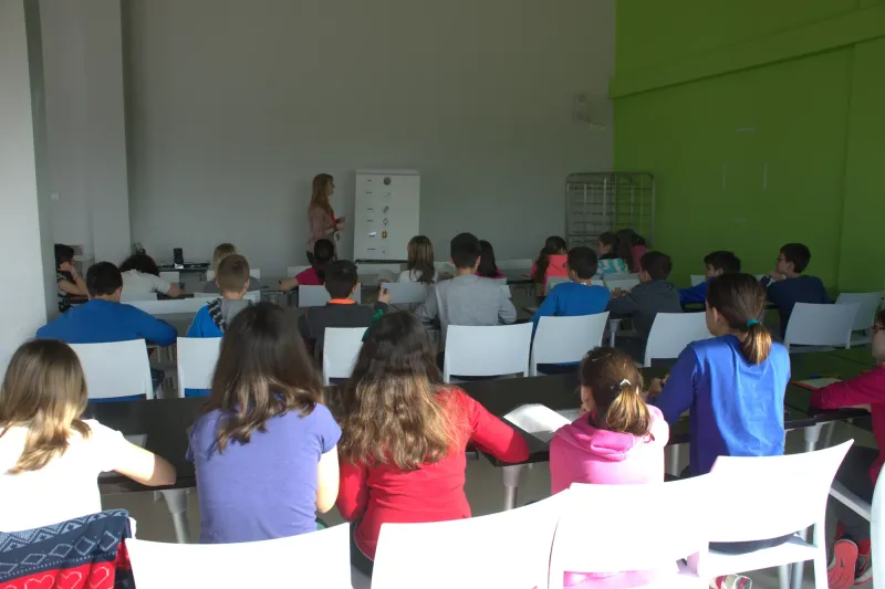 Alumnos de espaldas siguen la clase de inglés en un aula de pared verde